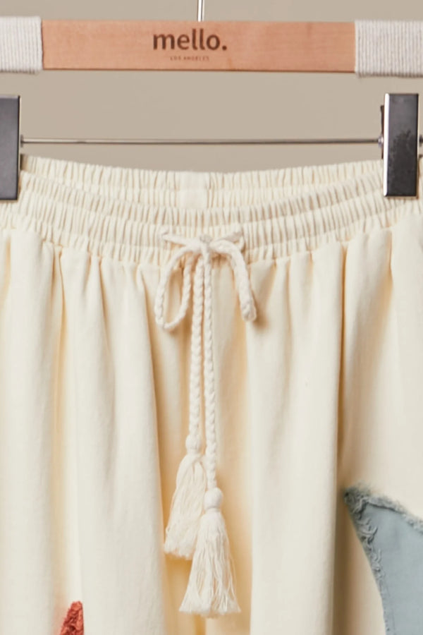 Cream wide leg lounge pants with sun, moon, and star print, styled with rust cardigan and light blue crop top outdoors - 4