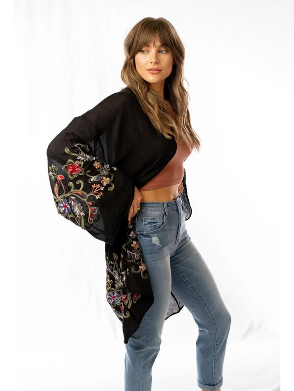 Woman wearing black floral embroidered kimono cardigan with wide sleeves over rust crop top and jeans - 3