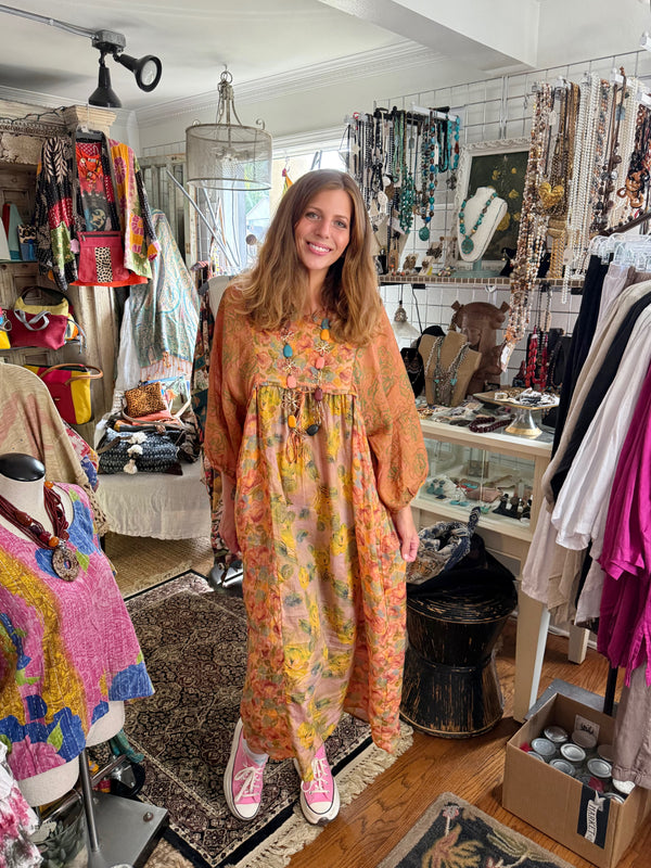 Woman wearing DYM90081 Bloomspell Maxi Dress in orange floral print with pink Converse sneakers in boutique setting - 1
