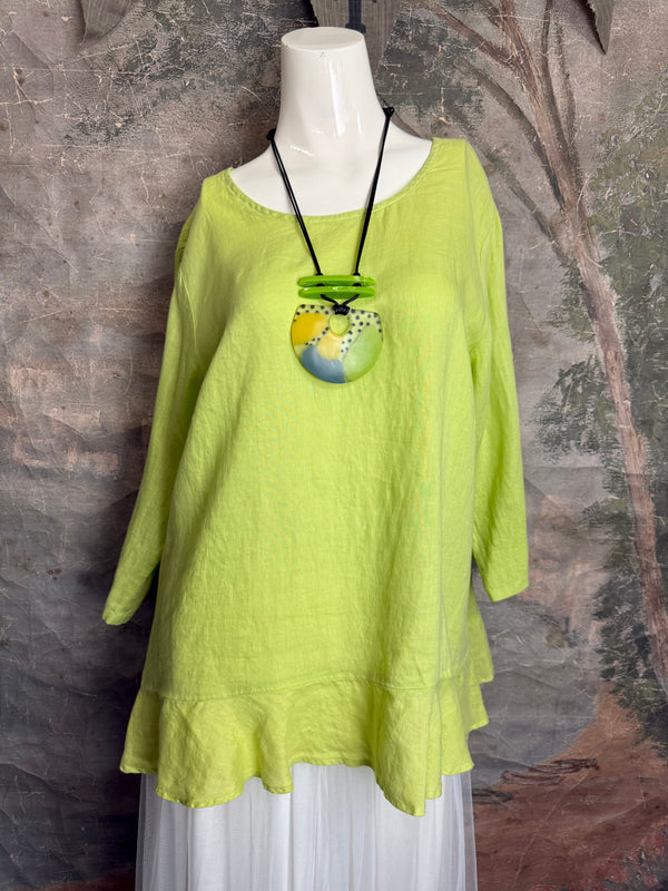 Mannequin wearing a green top with a colorful pendant against a textured wall.