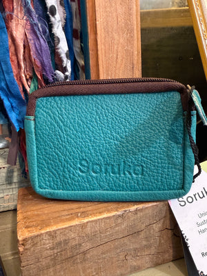 Teal leather coin pouch with spotted cowhide panel, brown zipper, and wrist strap on rustic wood display - 2