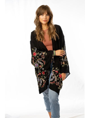Woman wearing black floral embroidered kimono cardigan with wide sleeves over rust crop top and jeans - 2