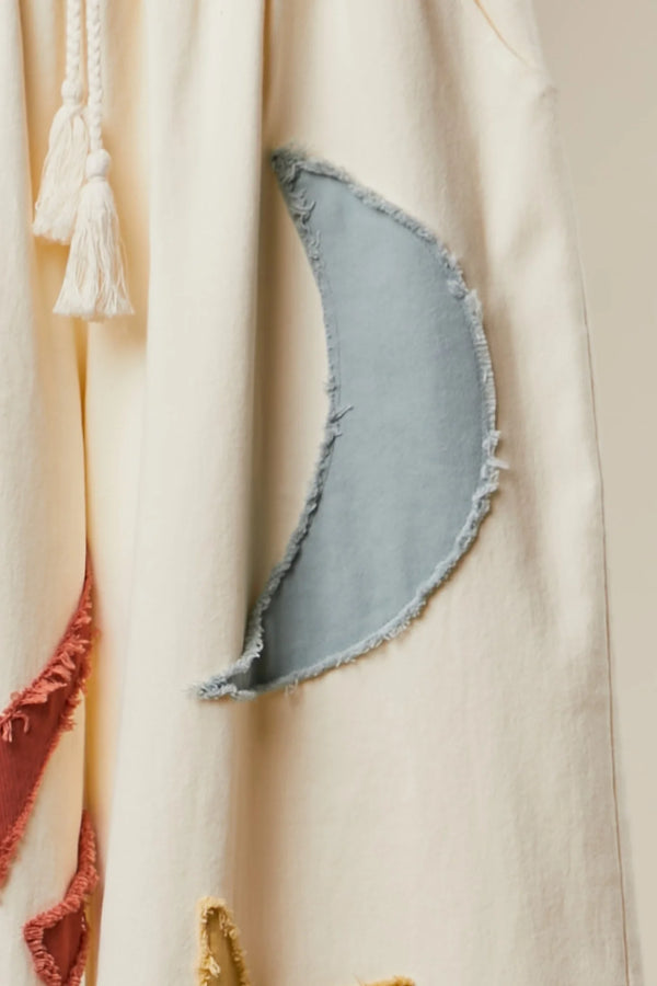 Cream wide leg lounge pants with sun, moon, and star print, styled with rust cardigan and light blue crop top outdoors - 3