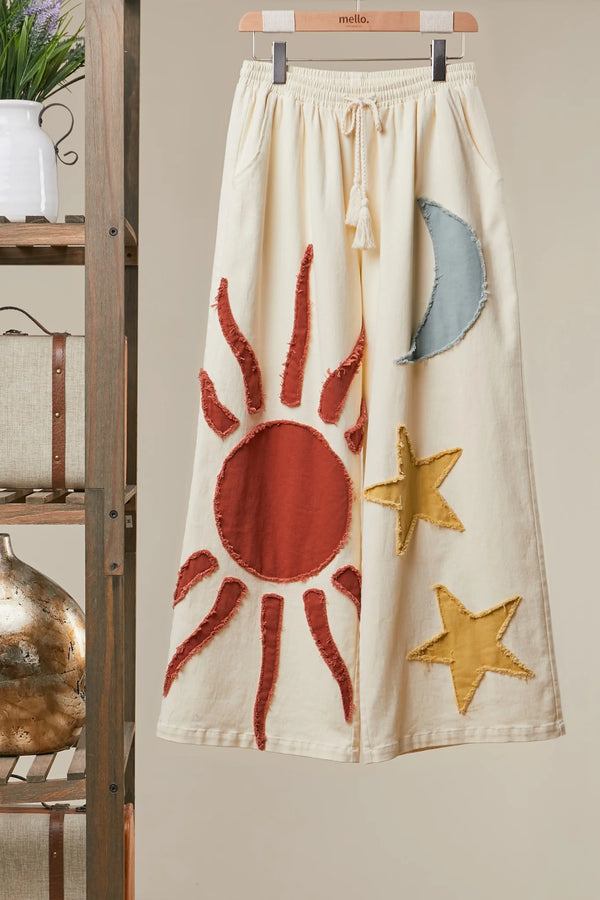 Cream wide leg lounge pants with sun, moon, and star print, styled with rust cardigan and light blue crop top outdoors - 6