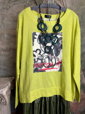 Lime green knit top with Never Grow Up graphic print, styled with green chain ring necklace and olive pleated skirt - 1