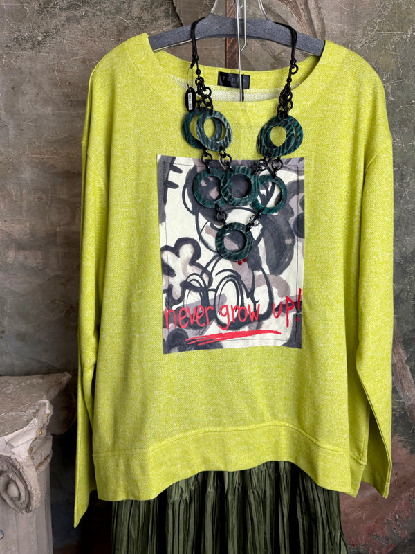 Lime green knit top with Never Grow Up graphic print, styled with green chain ring necklace and olive pleated skirt - 1