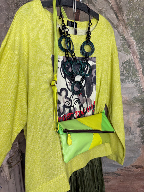 Lime green knit top with Never Grow Up graphic print, styled with green chain ring necklace and olive pleated skirt - 3