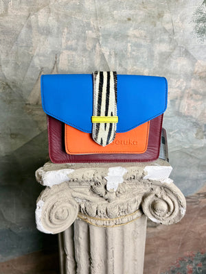 Goruka Grace Reversible Loop-B colorblock leather bag in blue, burgundy, orange with zebra print strap on stone column - 1