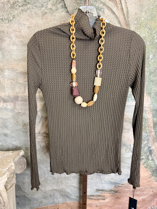Olive green waffle knit turtleneck long sleeve fitted top displayed with chunky beaded statement necklace on hanger - 1