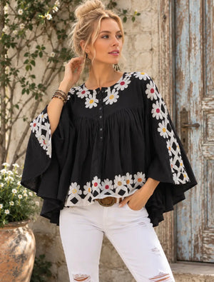 Black flowy boho blouse with white daisy embroidery, wide sleeves, button neckline, styled with white distressed jeans