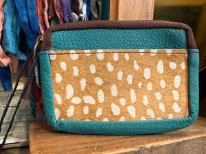 Teal leather coin pouch with spotted cowhide panel, brown zipper, and wrist strap on rustic wood display - 1
