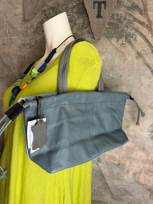 Gray leather shoulder bag with drawstring closure displayed on mannequin wearing lime green dress and colorful beaded ne - 1