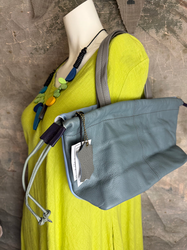 Gray leather shoulder bag with drawstring closure displayed on mannequin wearing lime green dress and colorful beaded ne - 2