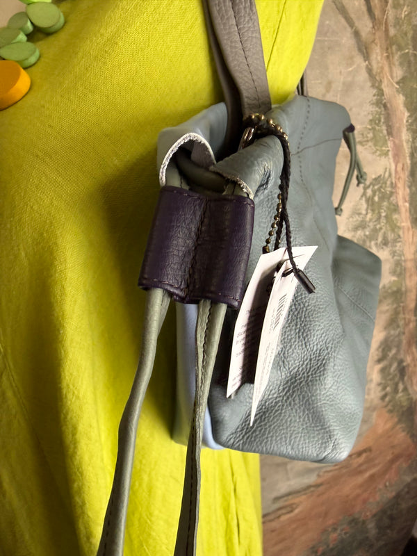 Gray leather shoulder bag with drawstring closure displayed on mannequin wearing lime green dress and colorful beaded ne - 5