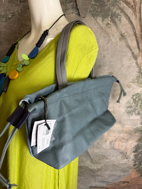 Gray leather shoulder bag with drawstring closure displayed on mannequin wearing lime green dress and colorful beaded ne - 6