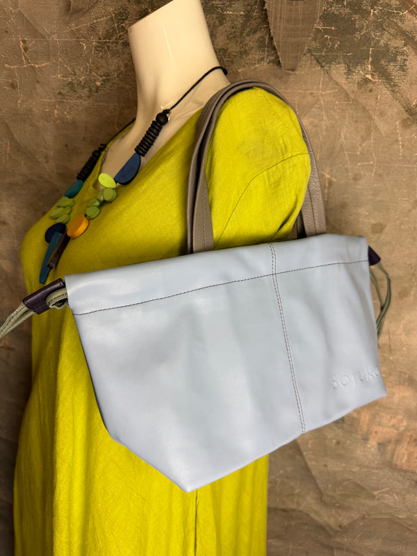 Gray leather shoulder bag with drawstring closure displayed on mannequin wearing lime green dress and colorful beaded ne - 8