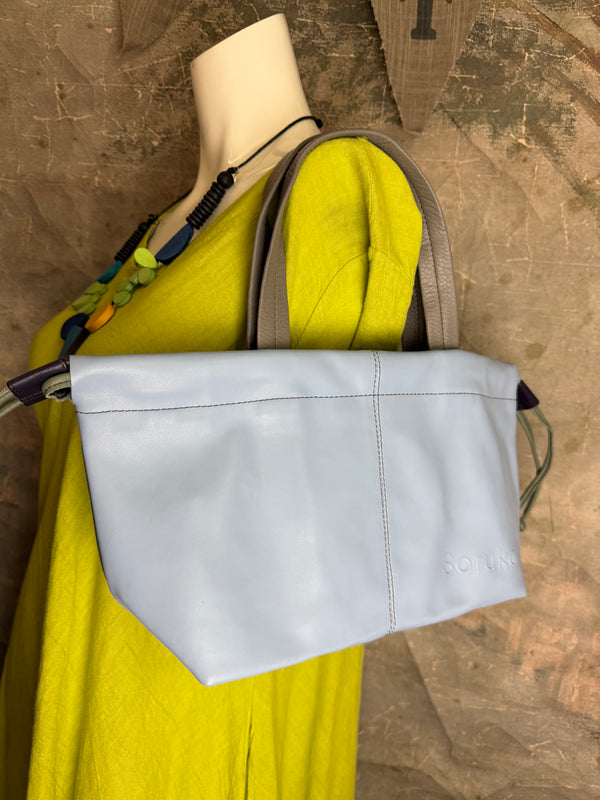 Gray leather shoulder bag with drawstring closure displayed on mannequin wearing lime green dress and colorful beaded ne - 13