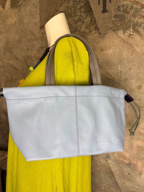 Gray leather shoulder bag with drawstring closure displayed on mannequin wearing lime green dress and colorful beaded ne - 14