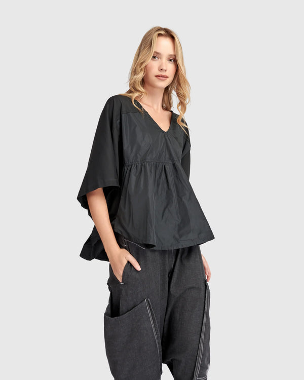 Woman wearing black taffeta butterfly top with flared sleeves and gathered waist paired with dark cargo pants - 1