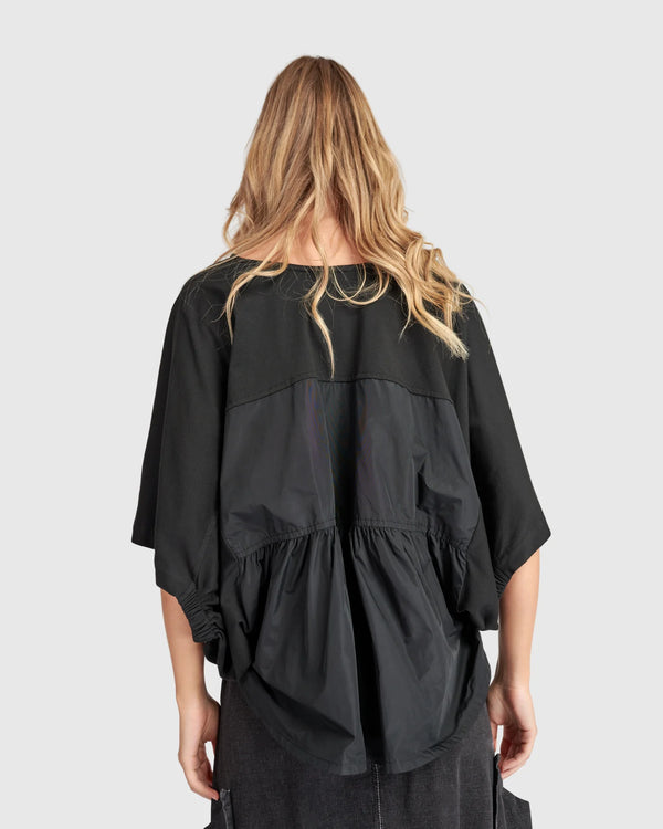 Woman wearing black taffeta butterfly top with flared sleeves and gathered waist paired with dark cargo pants - 3
