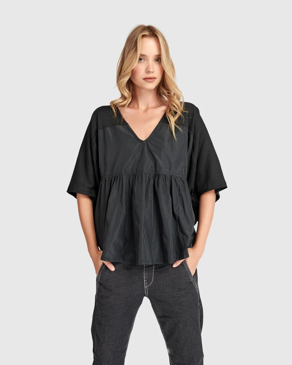 Woman wearing black taffeta butterfly top with flared sleeves and gathered waist paired with dark cargo pants - 2