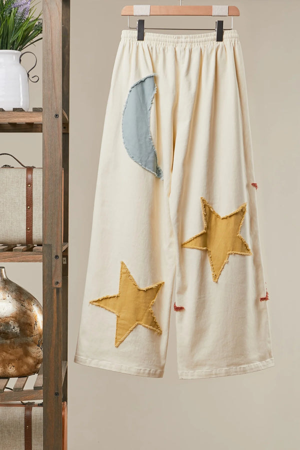 Cream wide leg lounge pants with sun, moon, and star print, styled with rust cardigan and light blue crop top outdoors - 5